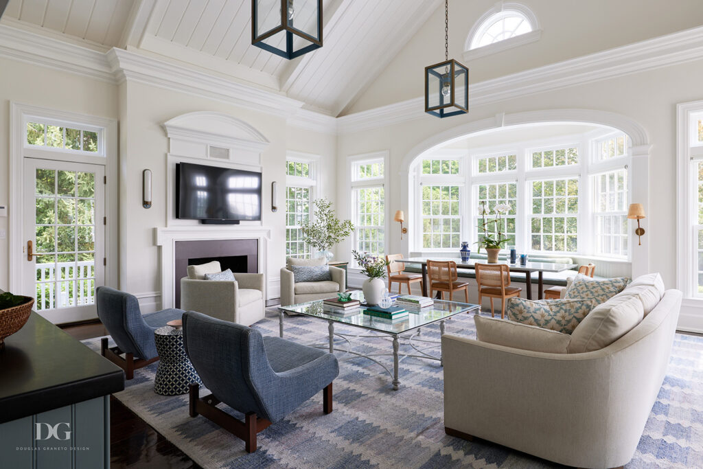 A white family room with vaulted ceiling, large bay window, fireplace, a Holly Hunt sofa, and a pair of blue Brazilian designed Espasso armchairs