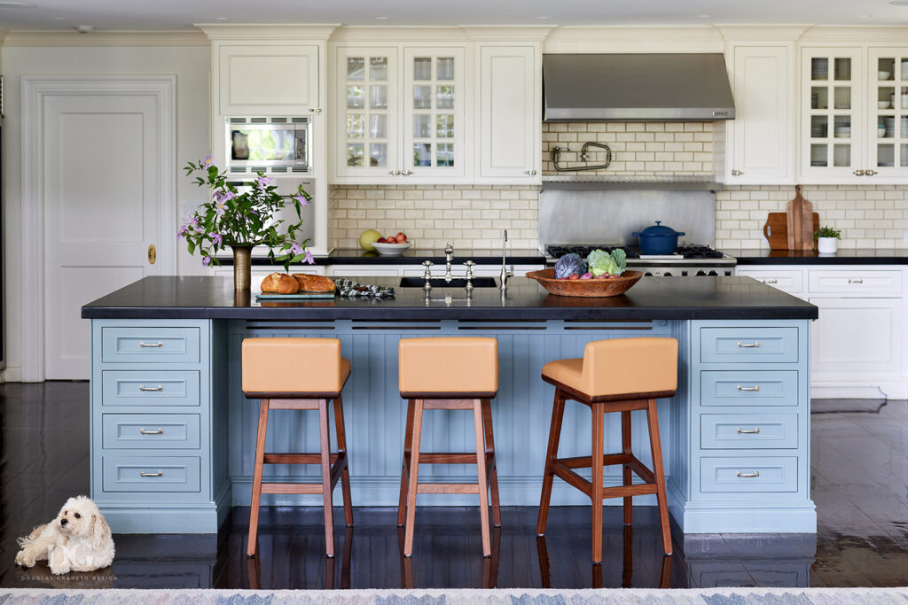 View of a kitchen island painted in a Farrow & Ball blue, with tan leather stools in front, and white painted wall cabinets behind
