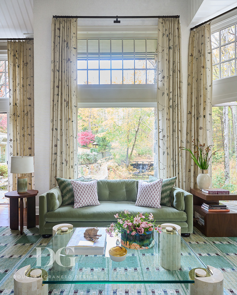 Living room with large windows and views of woodland. Green George Smith sofa, Karl Springer coffee table and Chelsea Editions curtains