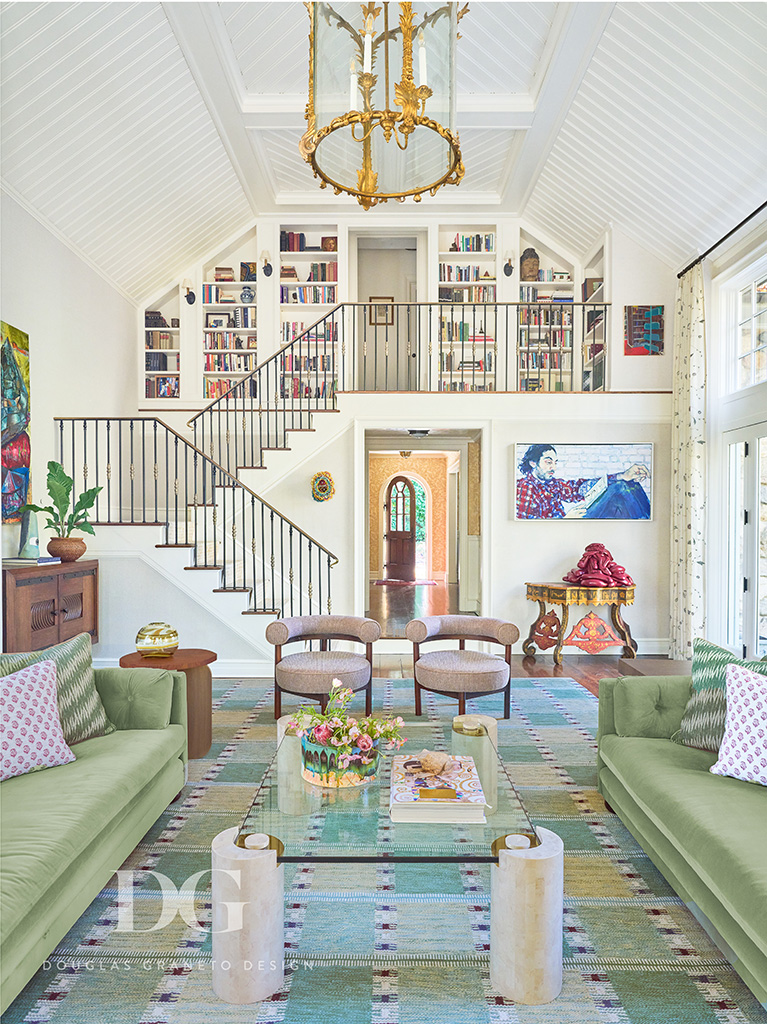 Living Room with green sofas and pink chairs looking through to a staircase leading to a mezzanine lined with bookcases. Karl Springer coffee table in the foreground.